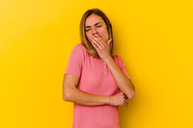 Joven mujer caucásica flaca aislada en amarillo bostezo mostrando un gesto cansado cubriendo la boca con la mano.