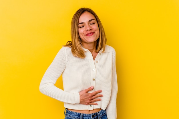 Foto joven mujer caucásica flaca aislada en la pared amarilla toca la barriga, sonríe suavemente, comiendo y concepto de satisfacción.