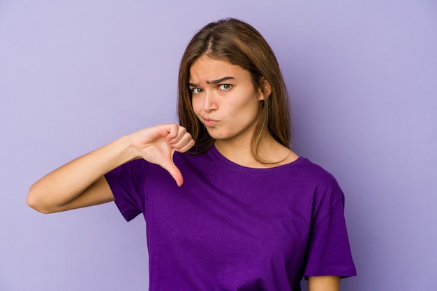 Joven mujer caucásica flaca en púrpura mostrando el pulgar hacia abajo, concepto de decepción.