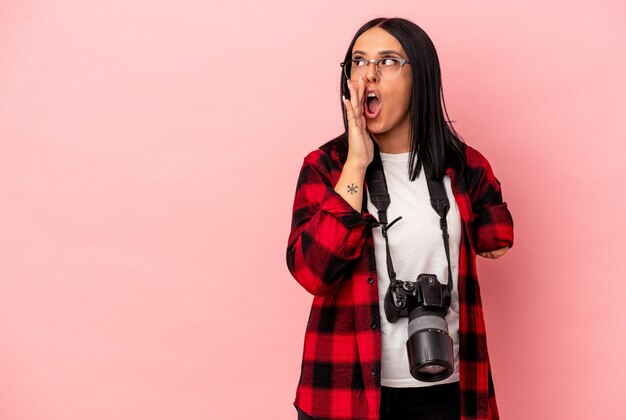 Joven mujer caucásica de fotografía con un brazo aislado sobre fondo rosa está diciendo una noticia secreta de frenado en caliente y mirando a un lado