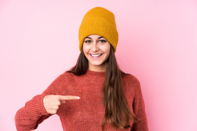 Joven mujer caucásica con una gorra de lana persona apuntando con la mano a una camisa copia espacio, orgulloso y confiado