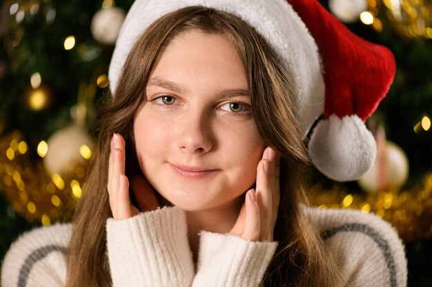 Joven mujer caucásica con gorro de Papá Noel sonríe en cámara, desea Navidad