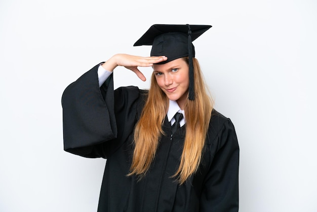 Joven mujer caucásica graduada de la universidad aislada de fondo blanco mirando lejos con la mano para mirar algo