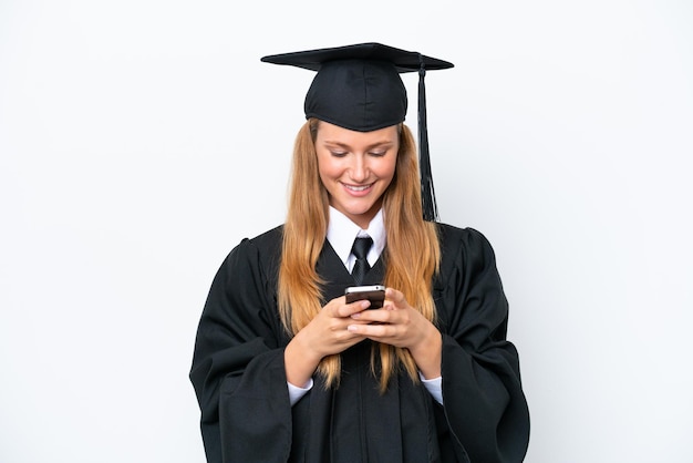 Joven mujer caucásica graduada de la Universidad aislada sobre fondo blanco enviando un mensaje con el móvil
