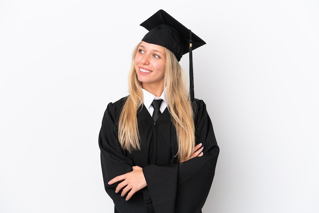 Joven mujer caucásica graduada de la universidad aislada sobre fondo blanco mirando hacia el lado