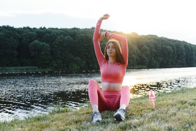 Joven mujer caucásica haciendo ejercicio de entrenamiento activo en una estera de yoga cerca del río en verano. Concepto de estilo de vida saludable