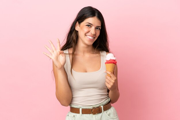 Joven mujer caucásica con un helado de cucurucho aislado sobre fondo rosa feliz y contando cuatro con los dedos