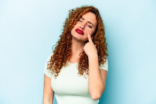 Joven mujer caucásica de jengibre aislada de fondo azul llorando infeliz con algo concepto de agonía y confusión