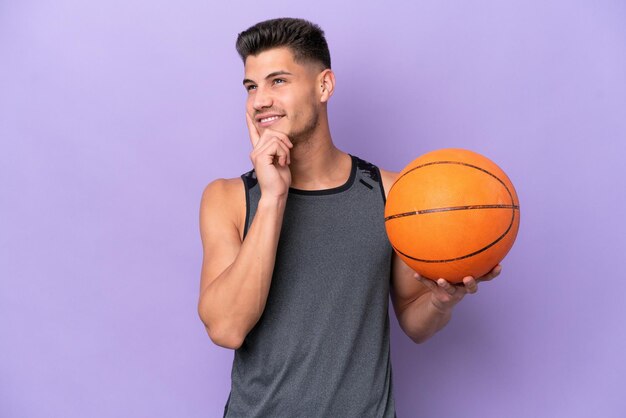 Joven mujer caucásica jugadora de baloncesto hombre aislado de fondo morado pensando en una idea mientras mira hacia arriba