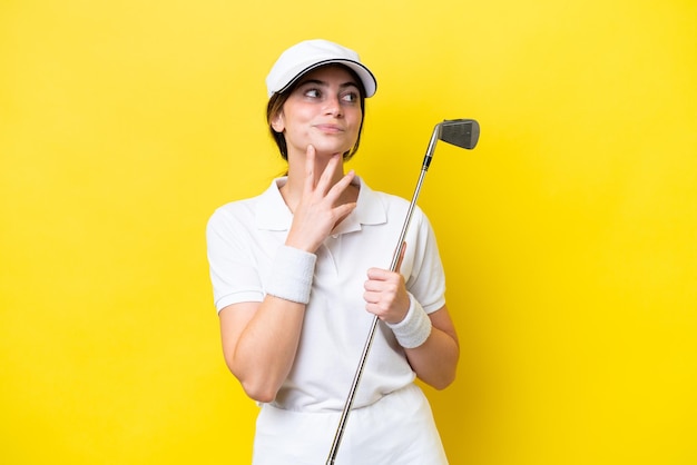 Joven mujer caucásica jugando al golf aislada de fondo amarillo con dudas y pensando