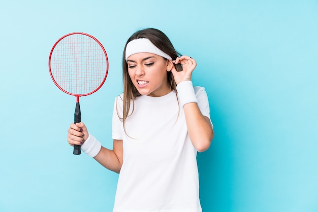 Joven mujer caucásica jugando bádminton aislado cubriendo las orejas con las manos.