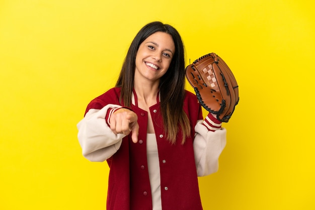 Joven mujer caucásica jugando béisbol aislado sobre fondo amarillo apuntando al frente con expresión feliz