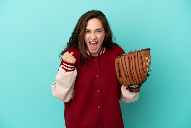 Joven mujer caucásica jugando béisbol aislado sobre fondo azul celebrando una victoria en la posición ganadora