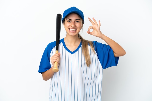 Joven mujer caucásica jugando béisbol aislado sobre fondo blanco mostrando signo ok con los dedos