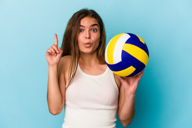 Joven mujer caucásica jugando voleibol aislado sobre fondo azul con una gran idea, concepto de creatividad.