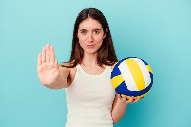 Joven mujer caucásica jugando voleibol aislado sobre fondo azul de pie con la mano extendida mostrando la señal de stop, impidiéndote.