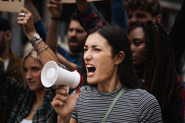 Joven mujer caucásica manifestante demuestra gritar fuerte a través del megáfono mientras está en una protesta