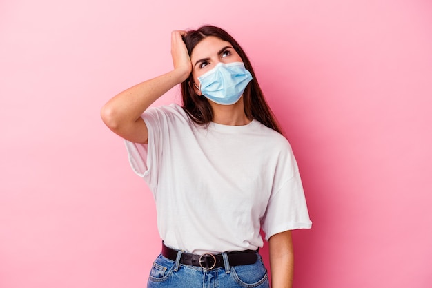 Joven mujer caucásica con una máscara para virus aislado en pared rosa cansada y con mucho sueño manteniendo la mano en la cabeza.