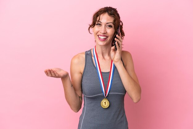 Joven mujer caucásica con medallas aisladas de fondo rosa manteniendo una conversación con alguien por teléfono móvil