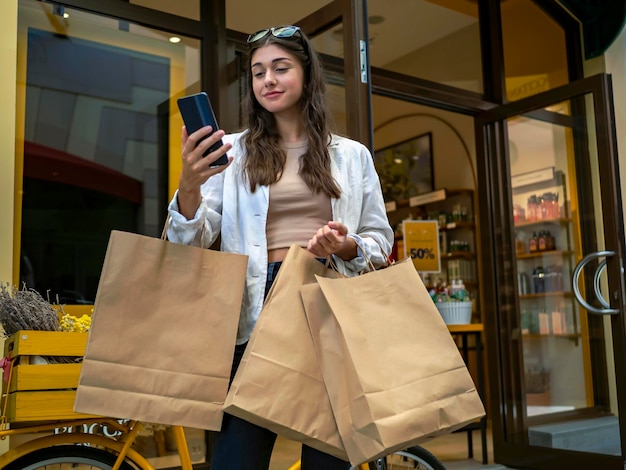 Joven mujer caucásica mirando su teléfono celular frente a la ventana de un centro comercial Black Friday