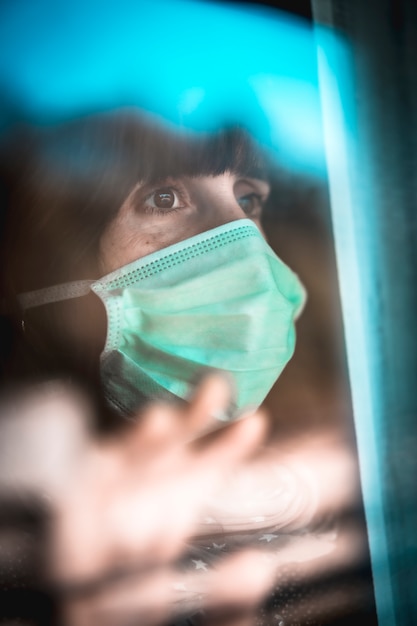 Una joven mujer caucásica mirando por la ventana en la cuarentena covid-19