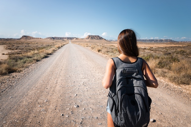 Joven mujer caucásica con una mochila gris caminando en medio de un postre en las Bardenas, Navarra, País Vasco.