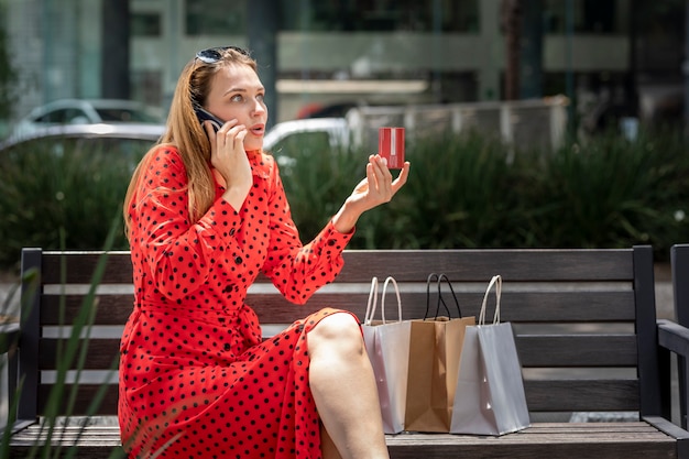 Joven mujer caucásica molesta en vestido rojo sentado en un banco hablando por teléfono para aclarar