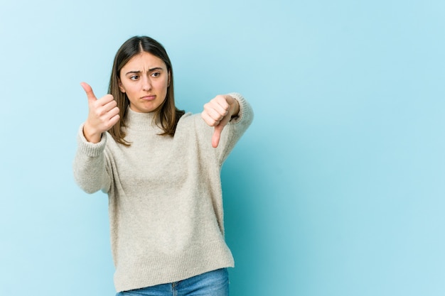 Joven mujer caucásica mostrando los pulgares hacia arriba y hacia abajo, difícil elegir el concepto