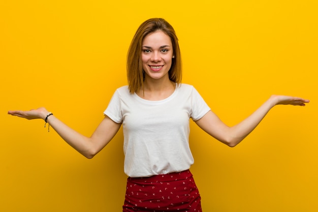 Joven mujer caucásica natural hace escala con los brazos, se siente feliz y confiada.