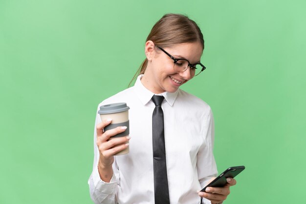 Joven mujer caucásica de negocios sobre un fondo aislado sosteniendo café para llevar y un móvil