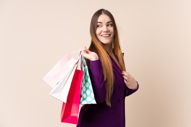 Joven mujer caucásica en pared beige sosteniendo bolsas de compras y sonriendo