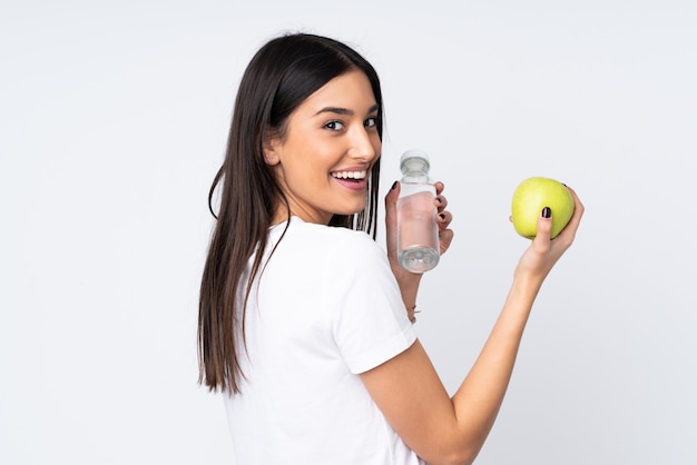 Joven mujer caucásica en pared blanca con una manzana y con una botella de agua