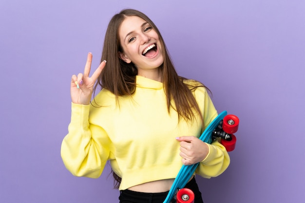 Joven mujer caucásica en pared púrpura con un patín con expresión feliz