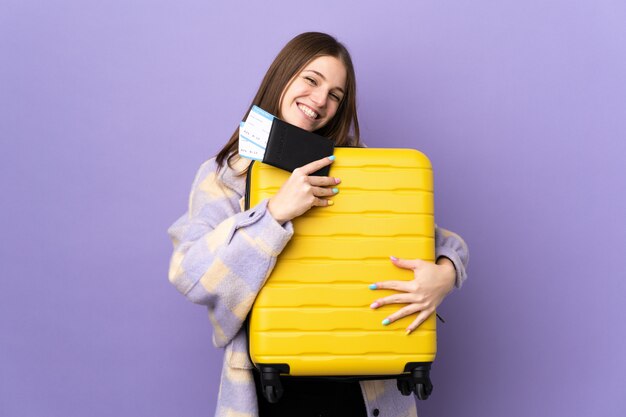 Joven mujer caucásica en pared púrpura en vacaciones con maleta y pasaporte