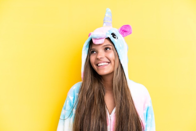 Joven mujer caucásica con un pijama de unicornio aislado en un fondo amarillo pensando en una idea mientras mira hacia arriba