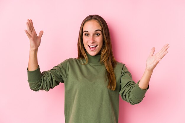 Joven mujer caucásica posando aislada recibiendo una agradable sorpresa, emocionada y levantando las manos.