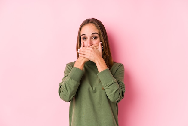 Joven mujer caucásica posando aislado sorprendido cubriendo la boca con las manos.