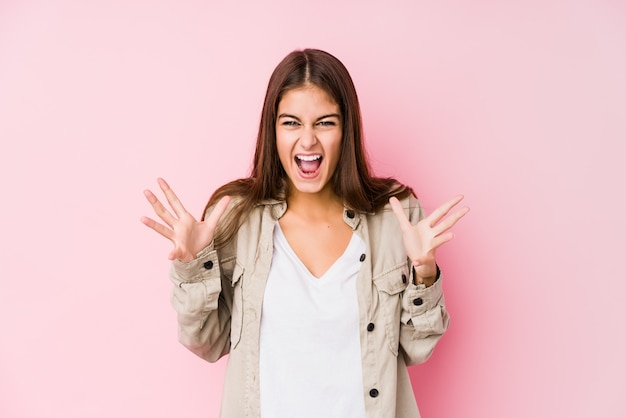 Joven mujer caucásica posando en una pared rosa celebrando una victoria o éxito, está sorprendido y conmocionado.