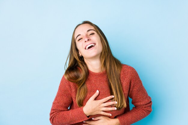 Joven mujer caucásica posando risas aisladas felizmente y se divierte manteniendo las manos sobre el estómago.