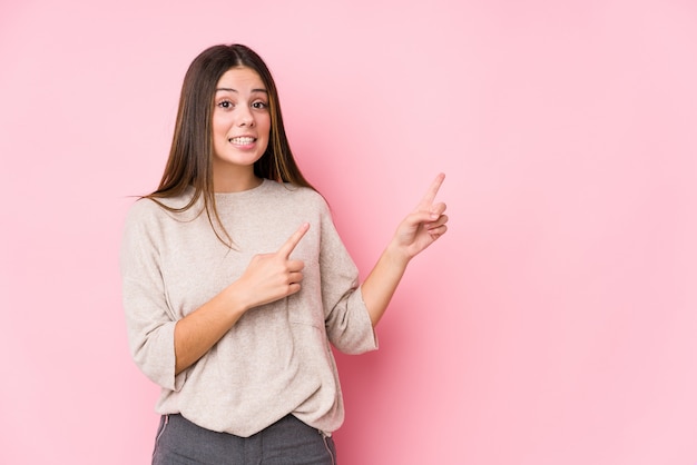 Joven mujer caucásica posando sorprendido señalando con los dedos índices a un espacio en blanco.