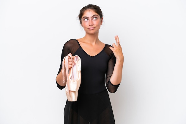 Joven mujer caucásica practicando ballet aislada de fondo blanco con los dedos cruzados y deseando lo mejor