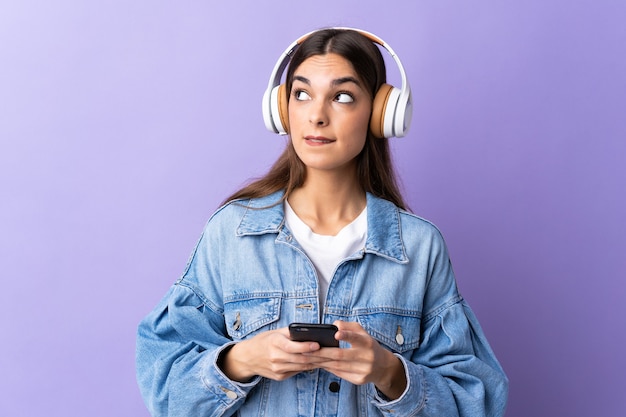 Joven mujer caucásica en púrpura escuchando música con un móvil y pensando