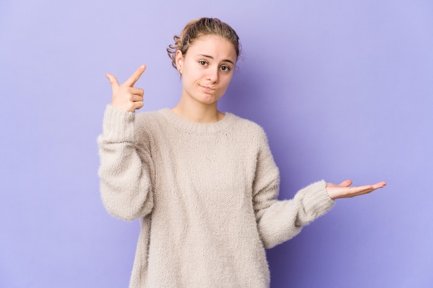 Joven mujer caucásica en púrpura sosteniendo y mostrando un producto a mano.