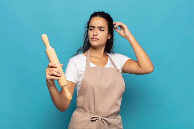 Joven mujer caucásica que se siente perpleja y confundida, rascándose la cabeza y mirando hacia un lado