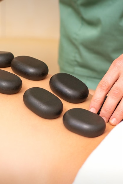 Joven mujer caucásica recibiendo masaje de espalda con piedras negras por masajista en el salón de spa