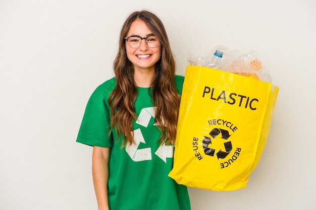 Joven mujer caucásica reciclando un lleno de plástico aislado sobre fondo blanco feliz, sonriente y alegre.