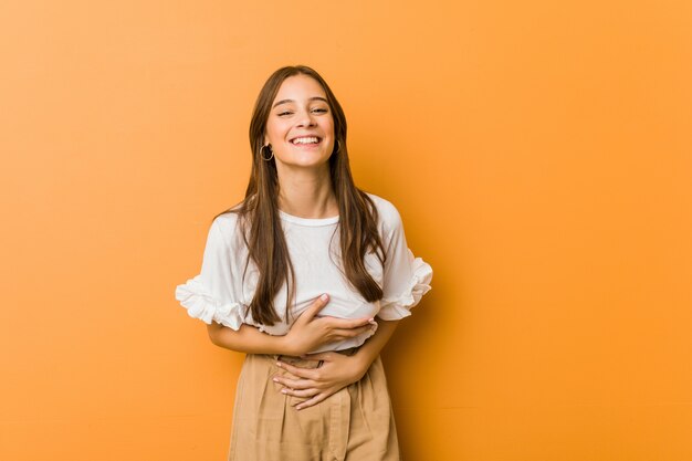 Joven mujer caucásica se ríe alegremente y se divierte manteniendo las manos sobre el estómago