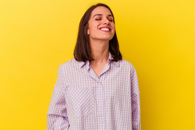 Joven mujer caucásica se ríe y cierra los ojos, se siente relajada y feliz.