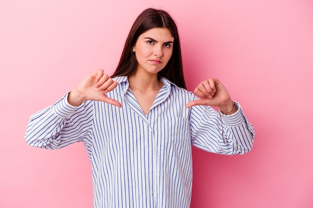 Joven mujer caucásica en rosa mostrando un gesto de aversión, pulgares hacia abajo. Concepto de desacuerdo.