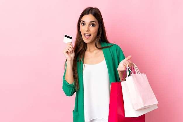 Joven mujer caucásica en rosa sosteniendo bolsas de compras y una tarjeta de crédito